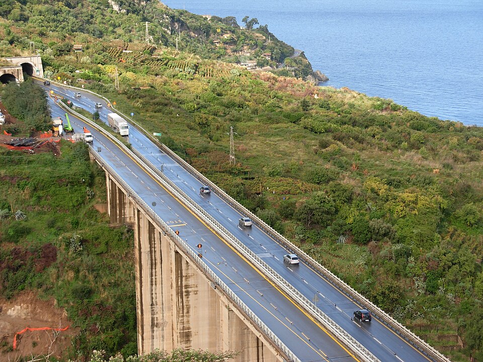 海沿いの斜面にかかる高速道路の高架を走るトラックと乗用車